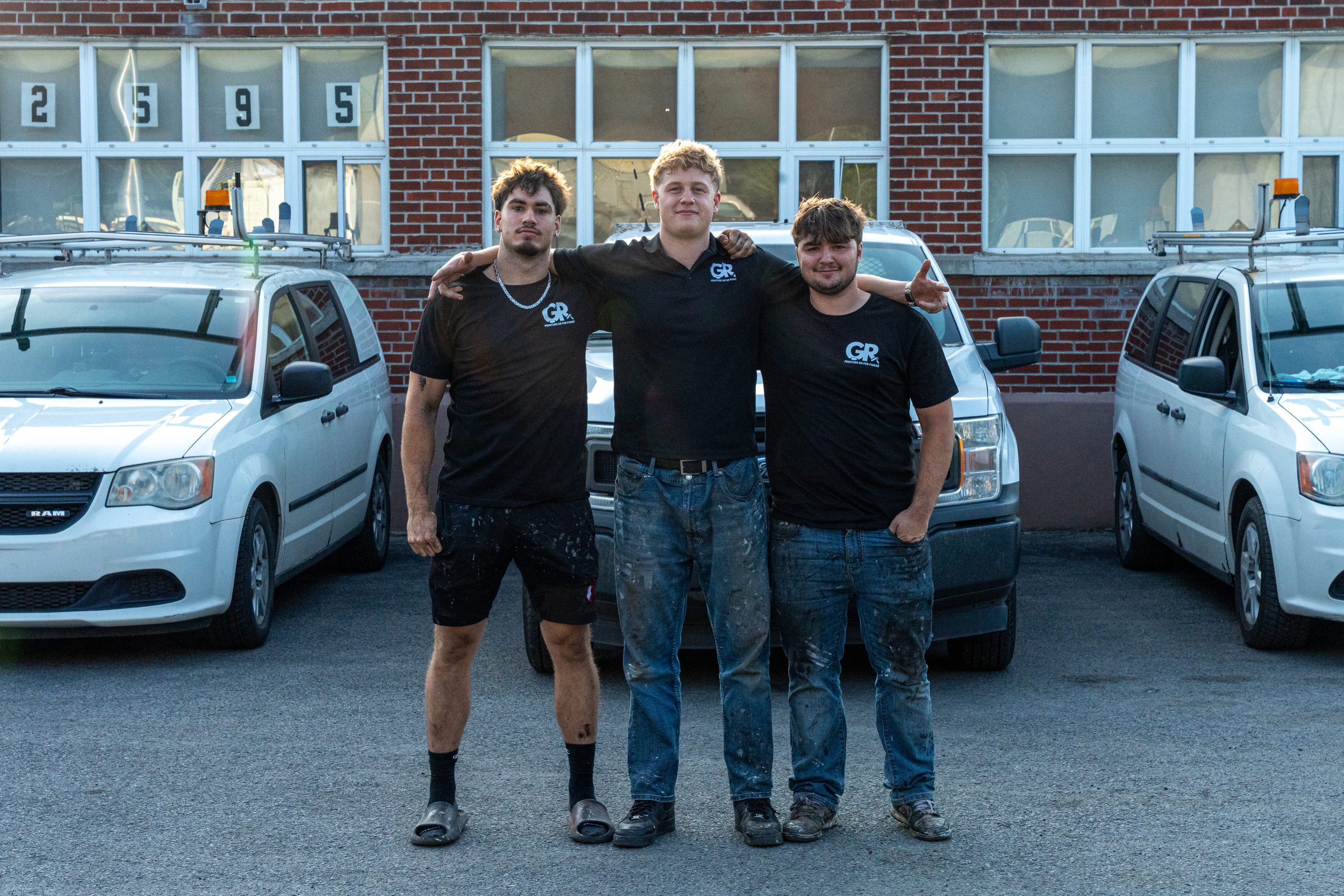 Trois membres de l'équipe Peinture GR, épaule contre épaule, devant les camions de l'entreprise